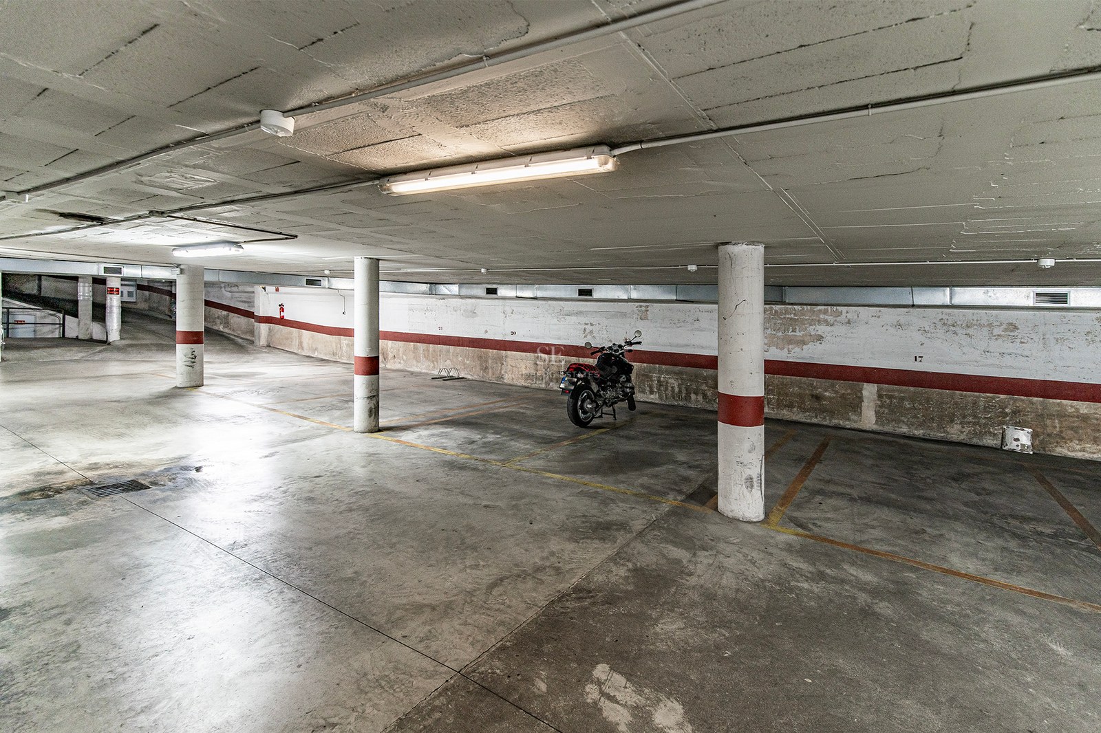 Underjordiskt betonggarage med numrerade parkeringsplatser, pelare och en parkerad motorcykel.
