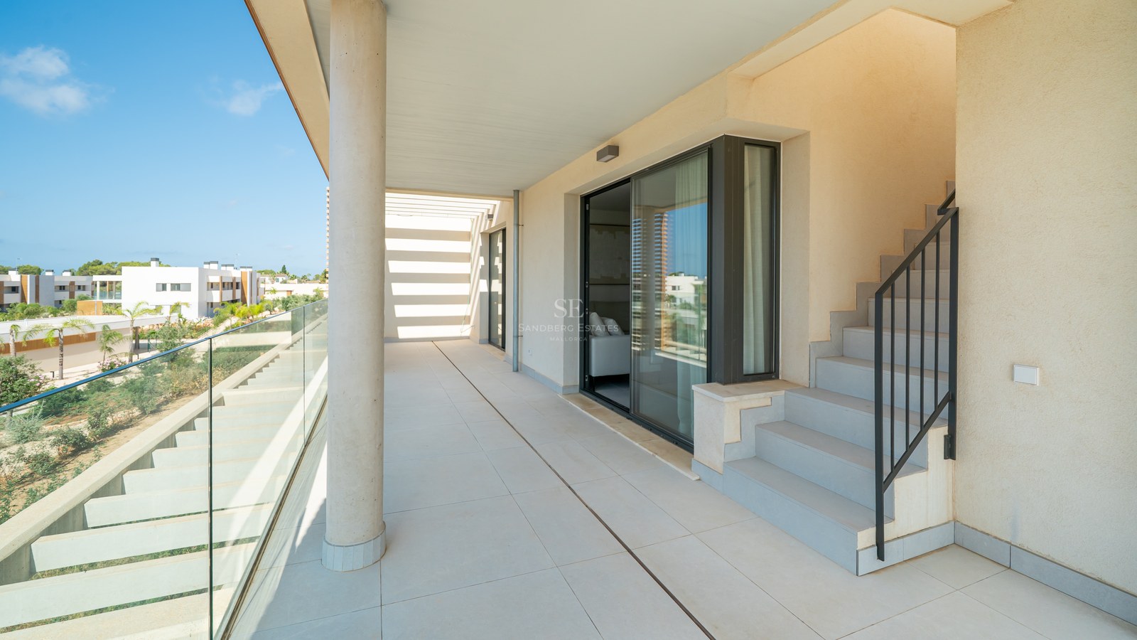 Spacious sun-drenched terrace with large format tiles, a glass railing, and outdoor stairs leading to an upper level.