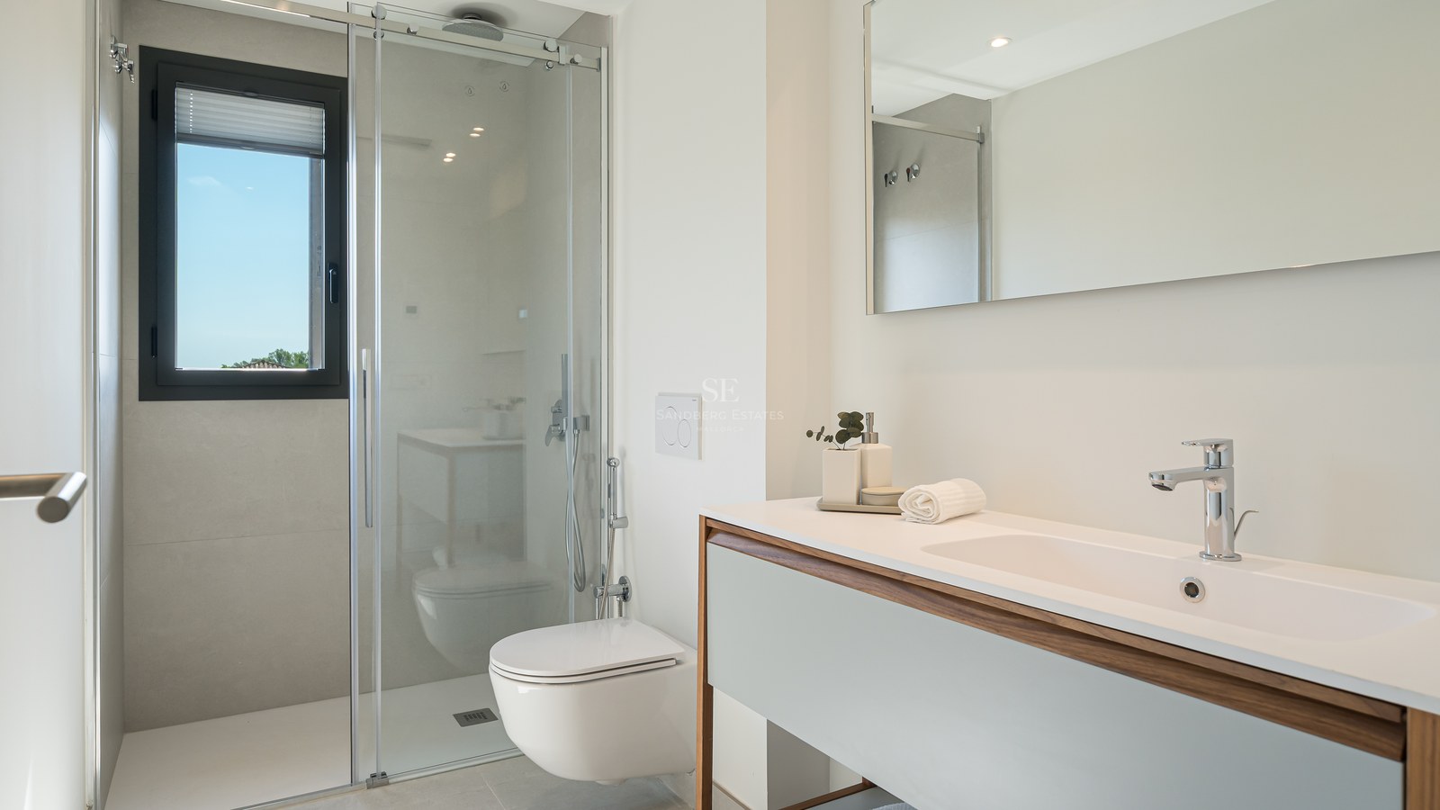 Bright bathroom featuring a glass walk-in shower, wall-mounted toilet, and white vanity with wood trim.