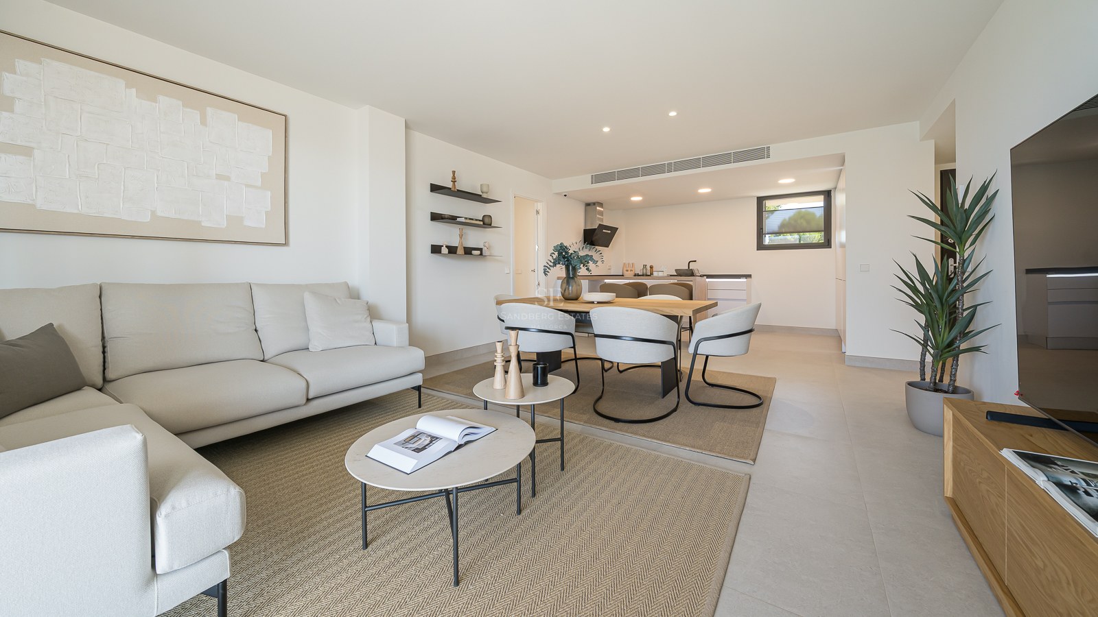 Bright living room with beige sofa, circular coffee tables, wooden dining set, and an integrated minimalist kitchen.