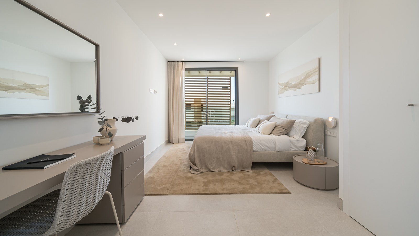 Bright modern bedroom with a large bed, integrated desk, floor-to-ceiling windows with wooden shutters, and neutral tones.