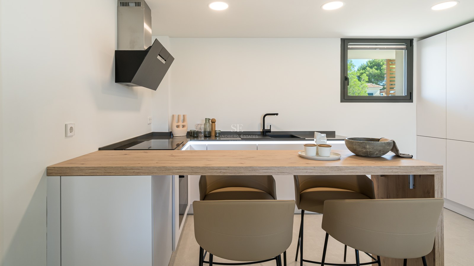 Contemporary white kitchen featuring a natural oak breakfast bar, black fixtures, and designer bar stools.