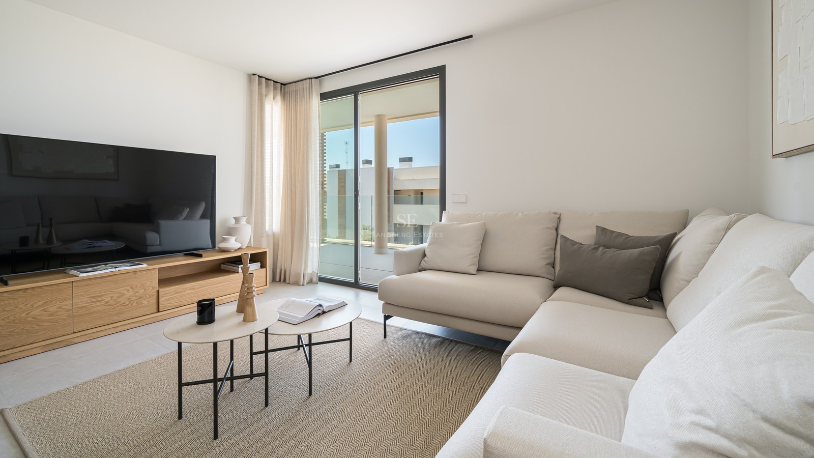 Bright living room featuring a cream L-shaped sofa, oak media unit, and sliding glass doors to a sunny terrace.