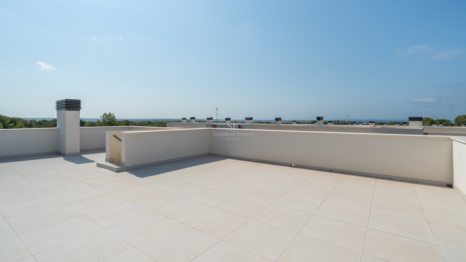 Large rooftop terrace with cream porcelain tiles and white plastered walls under a clear blue sky with sea views.