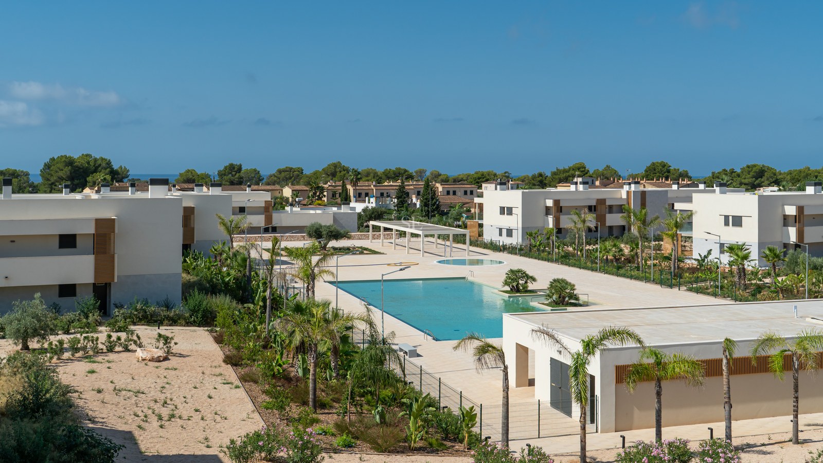 Elevated view of a large turquoise swimming pool within a modern residential complex with white buildings and palms.
