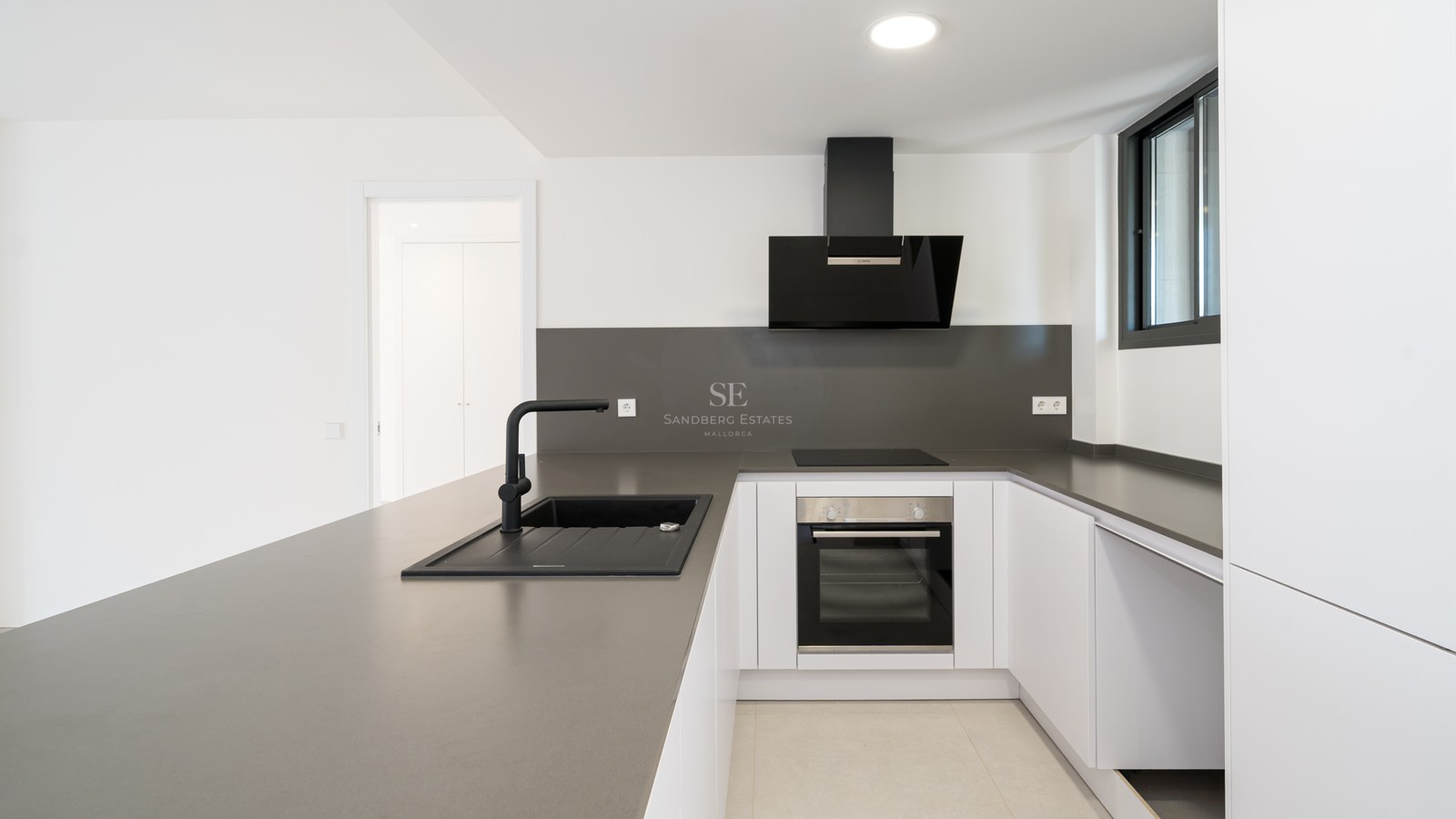 Clean white kitchen featuring grey quartz countertops, a black sink, and integrated Bosch appliances.