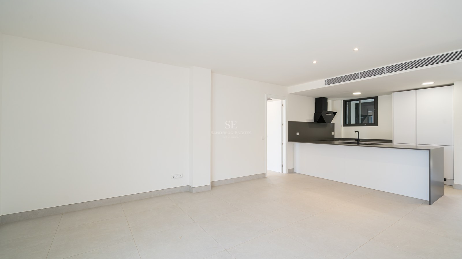 Clean minimalist kitchen with white cabinetry, dark countertops, and large grey floor tiles in an open living space.