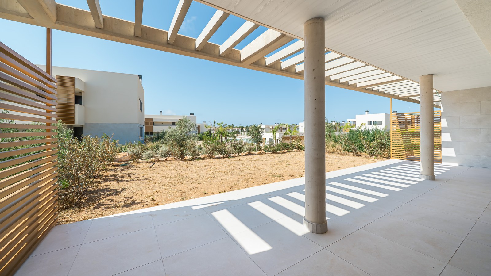 Expansive covered terrace featuring light porcelain tiles, concrete columns, and a wooden pergola under bright sunlight.