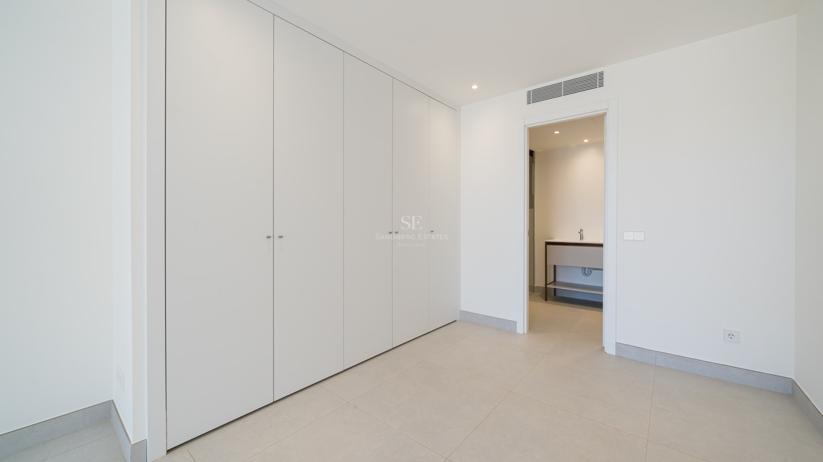 Minimalist white floor-to-ceiling built-in wardrobes in a bright room with an open door to a modern bathroom.