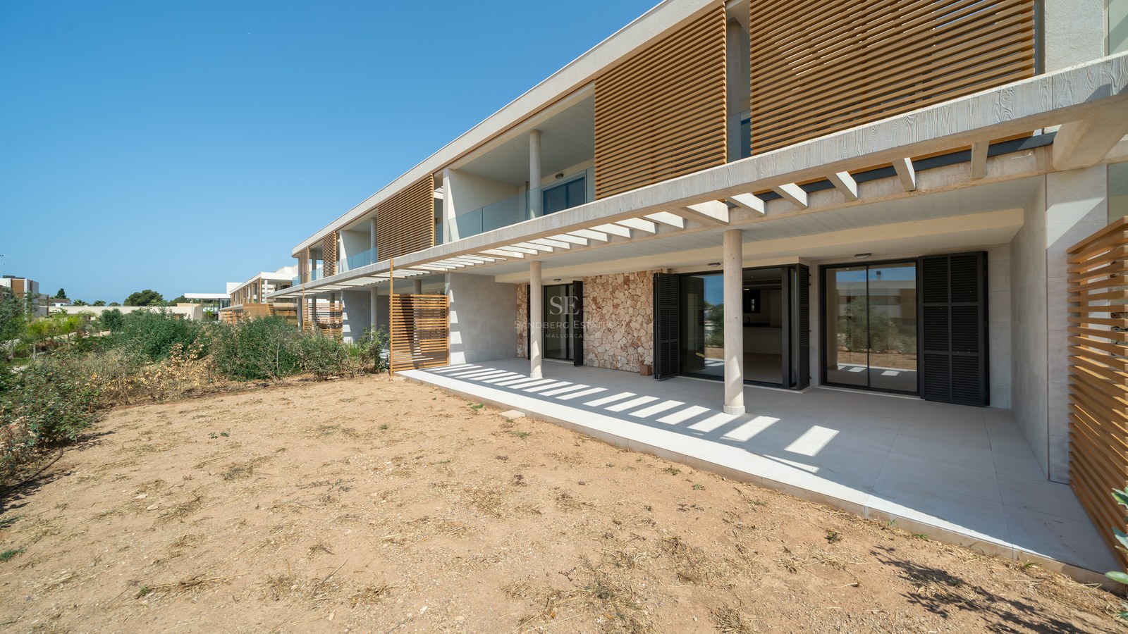 Modern residential facade featuring natural stone masonry, wooden slats, and a wide porcelain tile terrace.