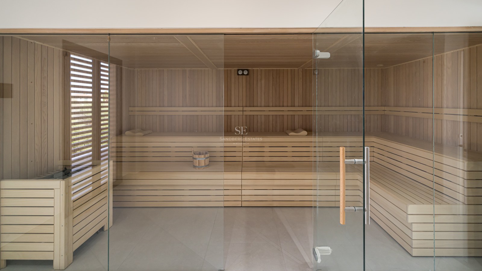 A spacious modern wood-paneled sauna featuring multi-level seating and a floor-to-ceiling glass entrance.