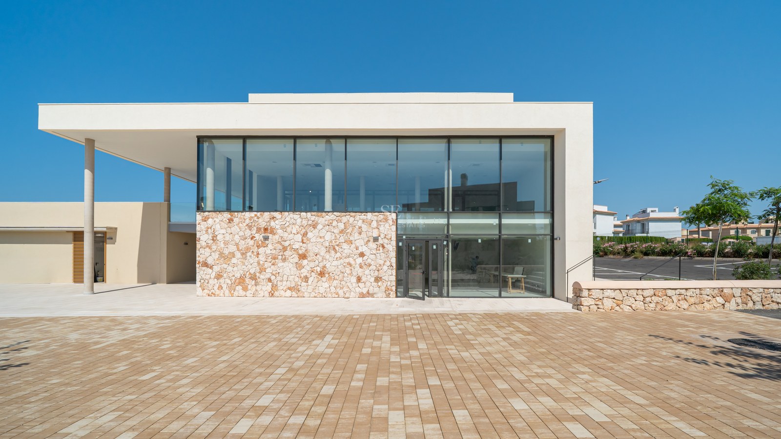 Modern building facade featuring large glass windows, a natural stone feature wall, and an expansive paved courtyard.