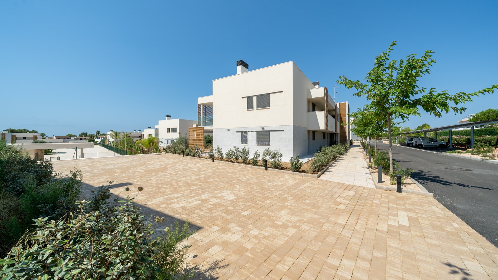 Exterior view of a modern white building with wooden accents and stone paving under a clear blue sky.