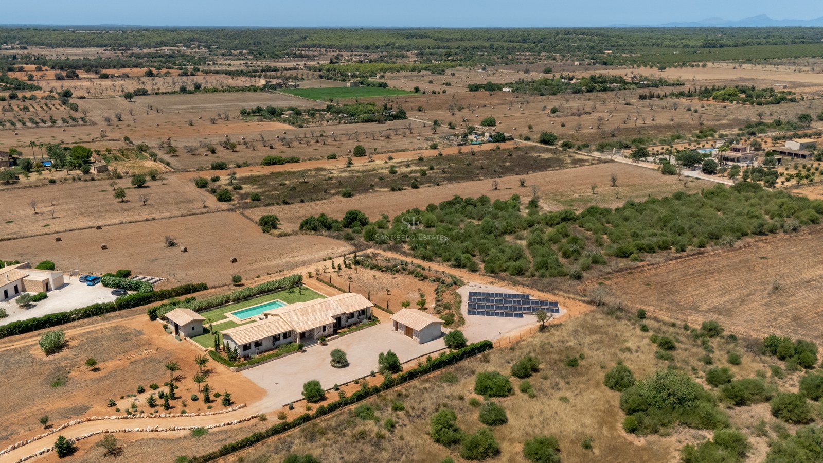 Vue aérienne d'une villa de luxe avec piscine et panneaux solaires dans un vaste paysage rural préservé.