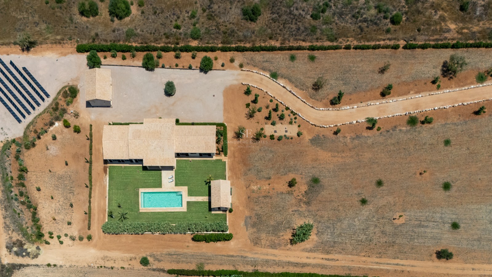 Vue aérienne d'une villa de luxe avec piscine, pelouse, panneaux solaires et vaste terrain naturel.