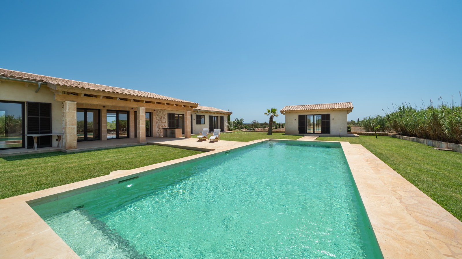 Une vaste piscine turquoise entourée d'une terrasse en pierre naturelle et d'une villa de style méditerranéen.