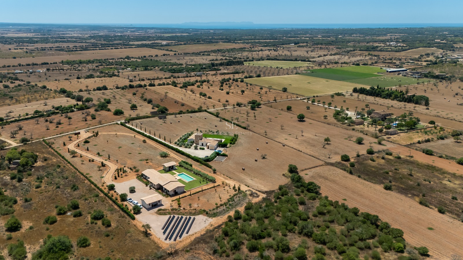 Vue aérienne d'une villa méditerranéenne de luxe avec piscine, grand terrain, panneaux solaires et vue mer lointaine.