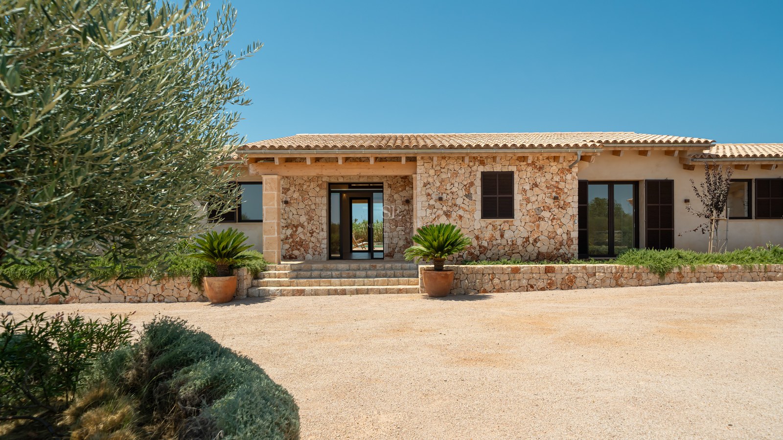 Entrée de villa de luxe avec murs en pierre naturelle, toit en terre cuite et allée en gravier.