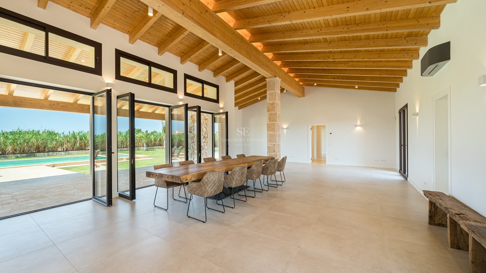 Grande salle à manger avec hauts plafonds en bois et baies vitrées pliantes ouvrant sur le jardin et la piscine.