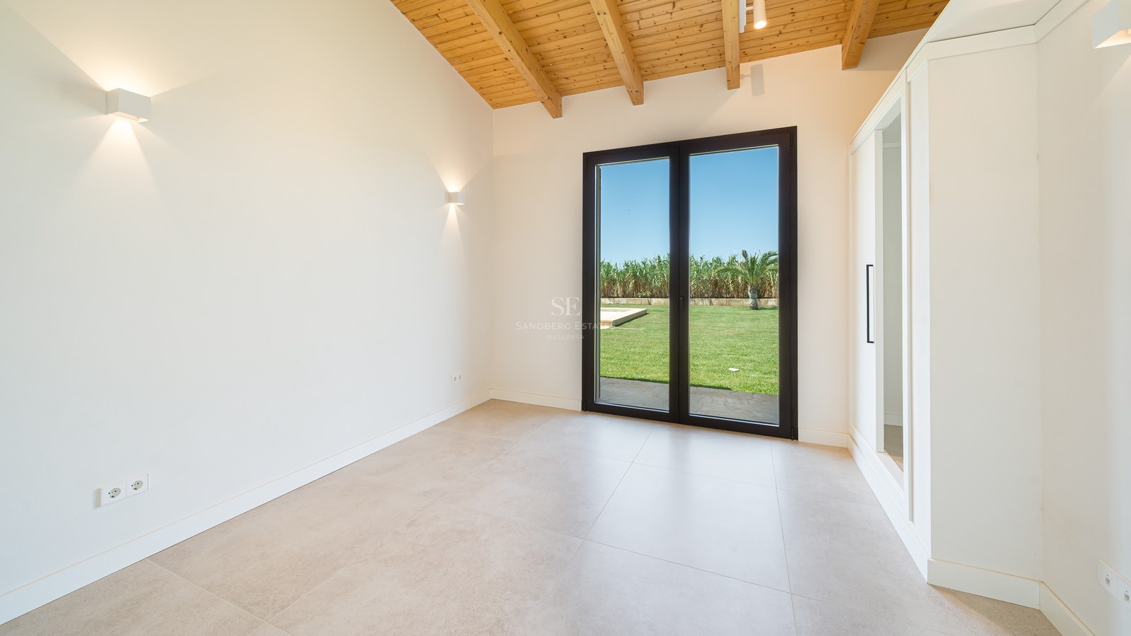 Chambre vide avec plafond voûté en bois, grandes baies vitrées ouvrant sur le jardin et placards blancs.