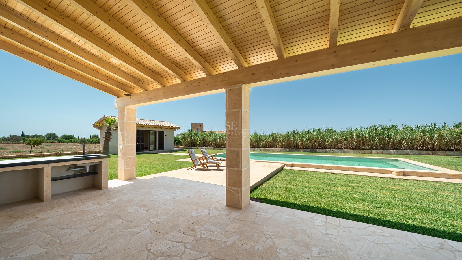 Terrasse couverte avec plafond en bois, évier extérieur et vue sur la piscine et le jardin.