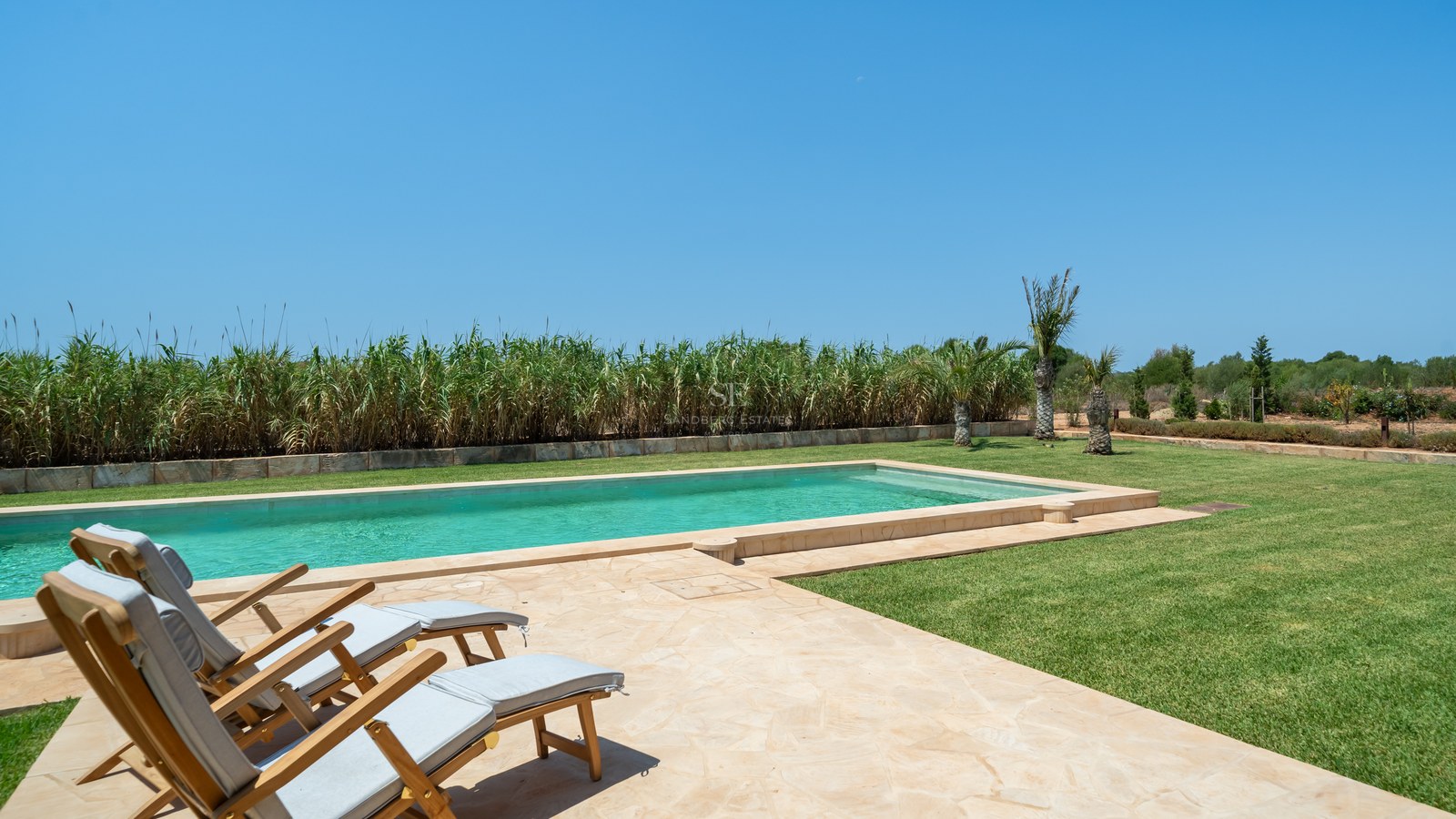Piscine rectangulaire aux eaux turquoises, terrasse en pierre naturelle, chaises longues en bois et pelouse soignée.