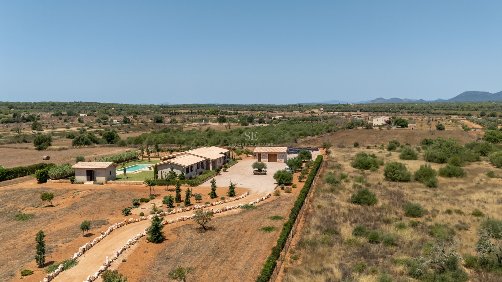 Vue aérienne d'une villa méditerranéenne moderne avec piscine et panneaux solaires entourée d'un vaste paysage rural.