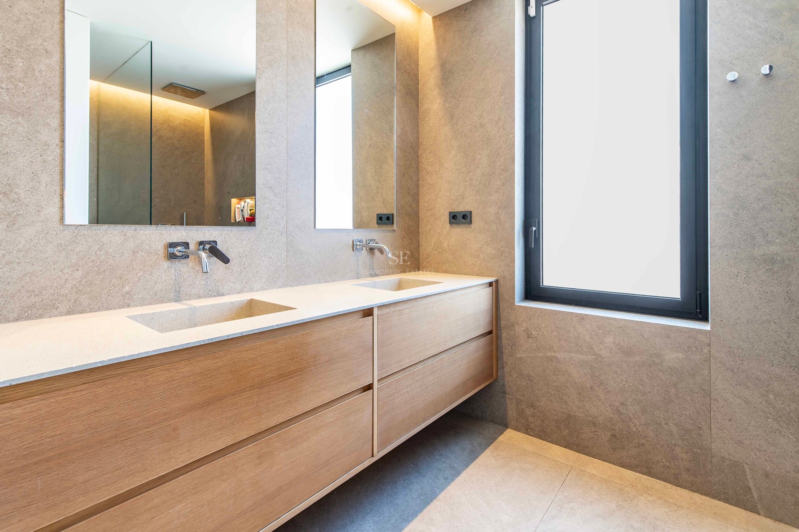 Luxury bathroom featuring a double wood vanity with integrated stone sinks and large mirrors against stone walls.