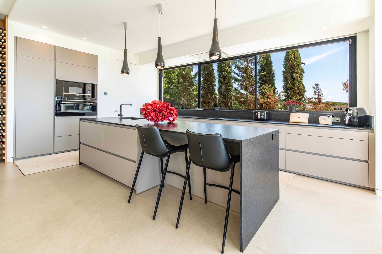 Modern minimalist kitchen featuring a charcoal stone island, handleless grey cabinets, and a wide panoramic window.