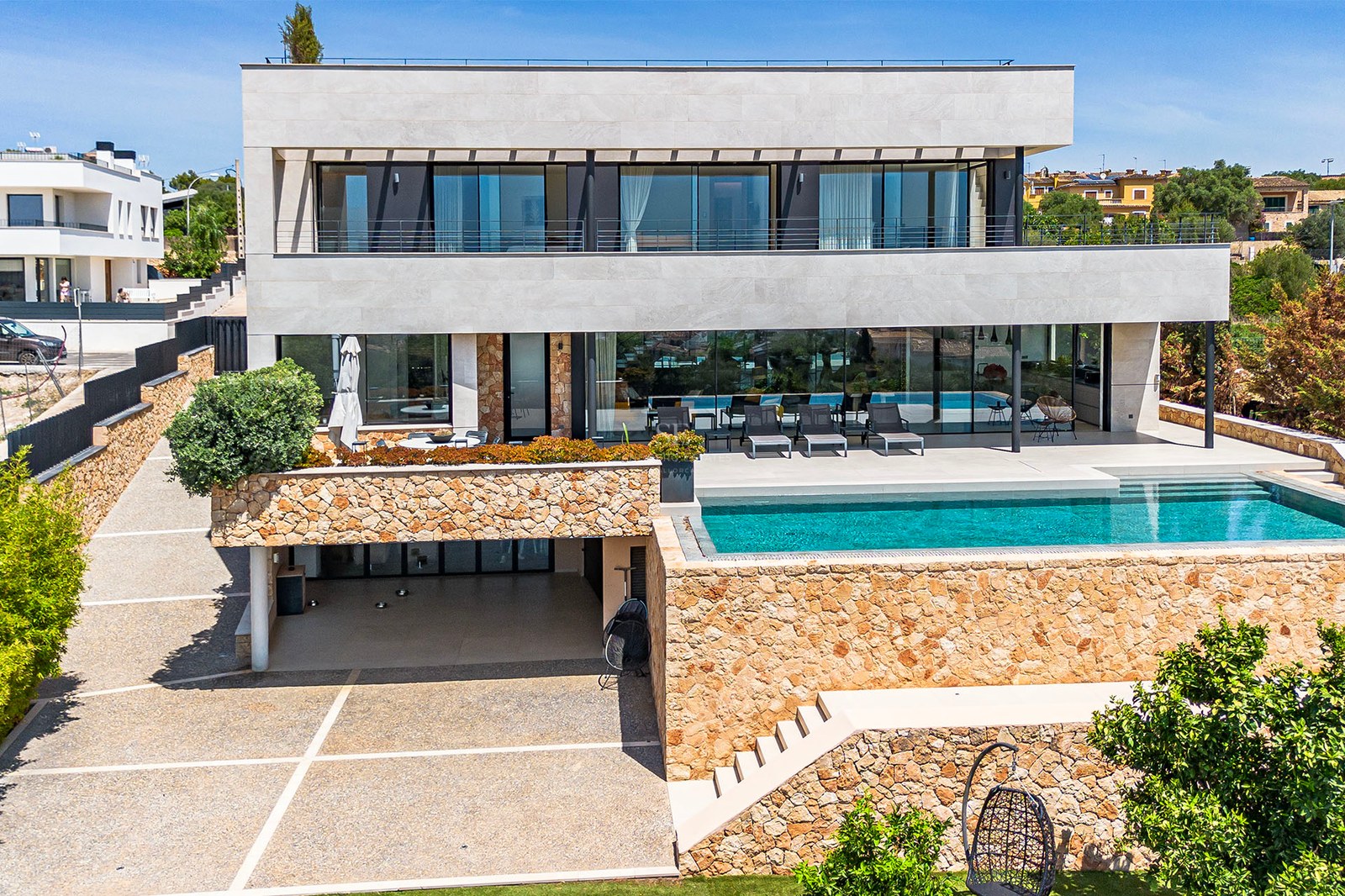 Exterior view of a three-story contemporary villa featuring natural stone walls, large glass windows, and a turquoise pool.