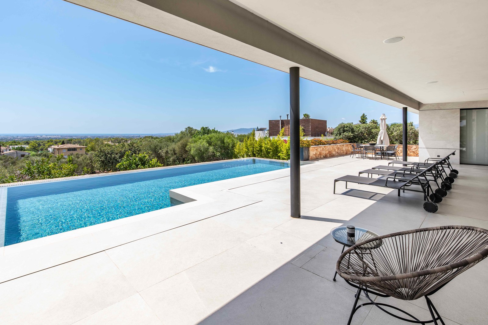Infinity pool on a white stone terrace with black loungers and panoramic views of the green valley and sea.