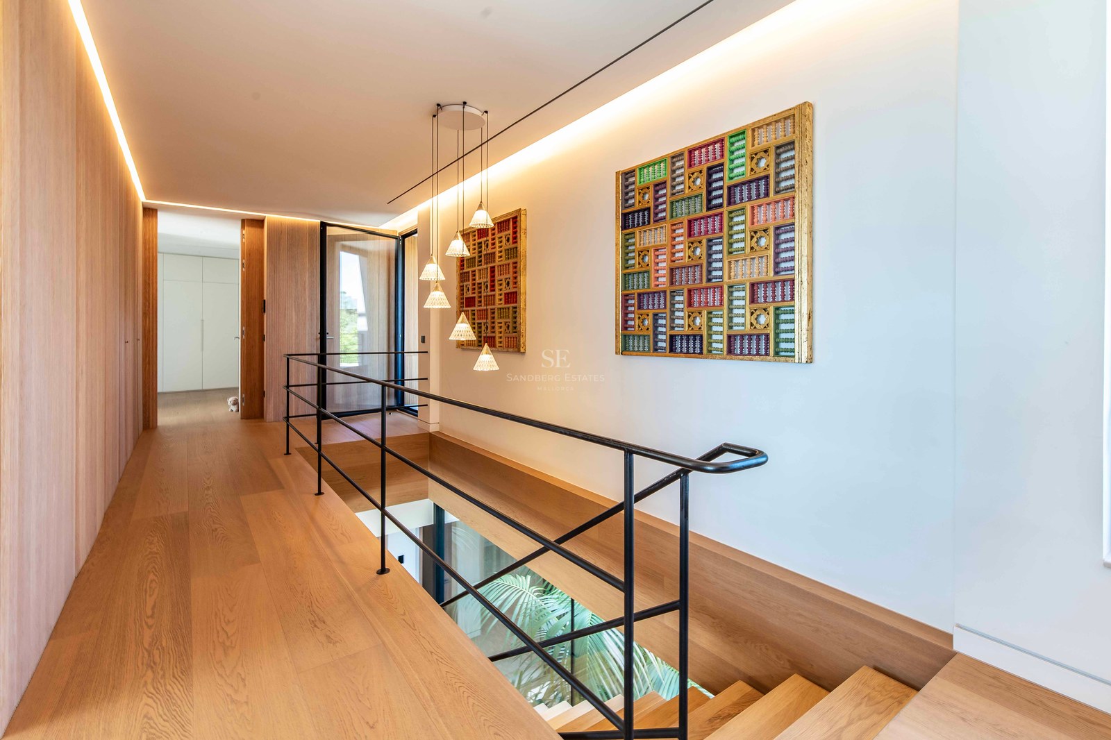 Modern hallway featuring oak flooring, black metal railings, and vibrant geometric wall art in a bright space.