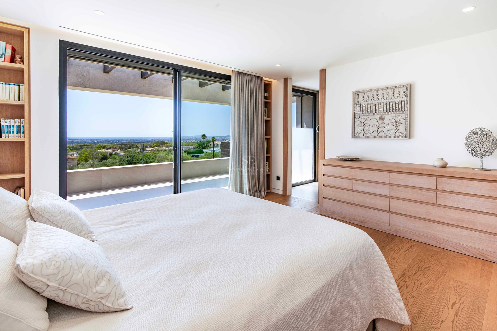 Modern bedroom featuring oak floors, light wood furniture, and glass doors opening to a terrace with sea views.