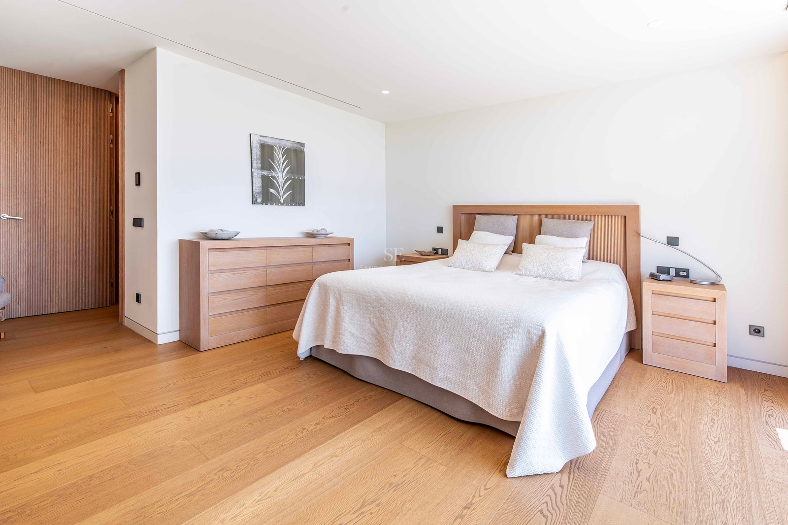 Bright modern bedroom featuring light oak flooring, a matching wood headboard, and minimalist white walls.