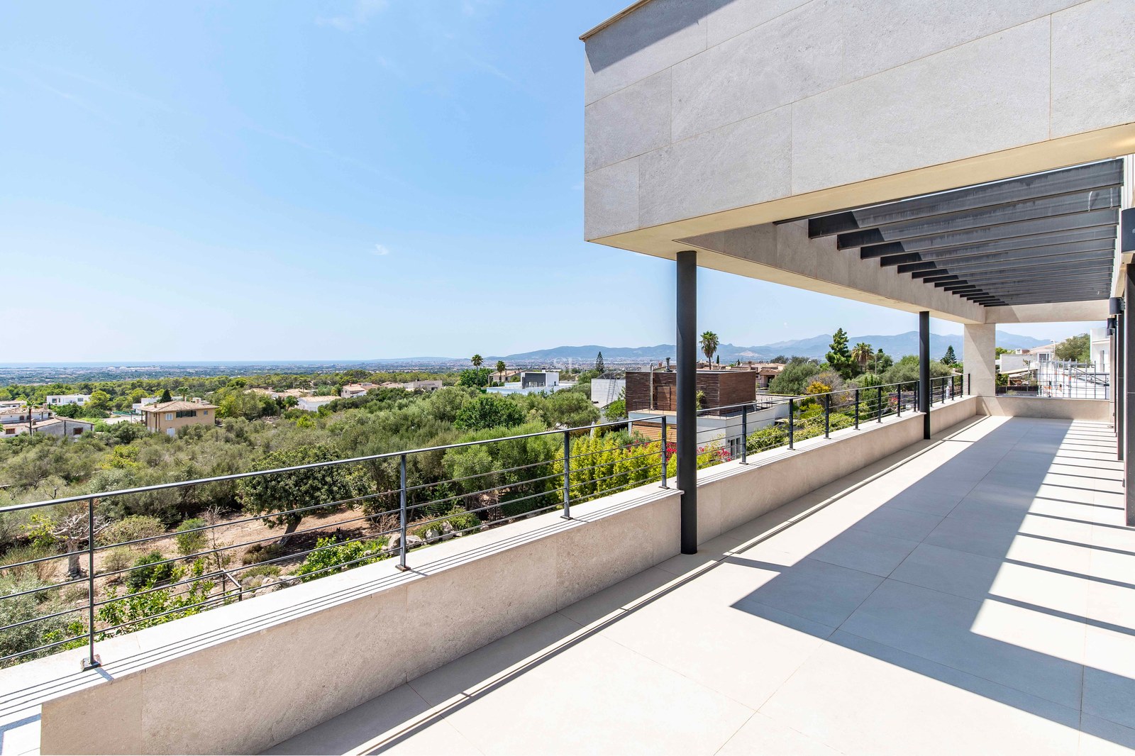 Large modern terrace with stone tiling and metal railings overlooking a green valley towards the Mediterranean sea.