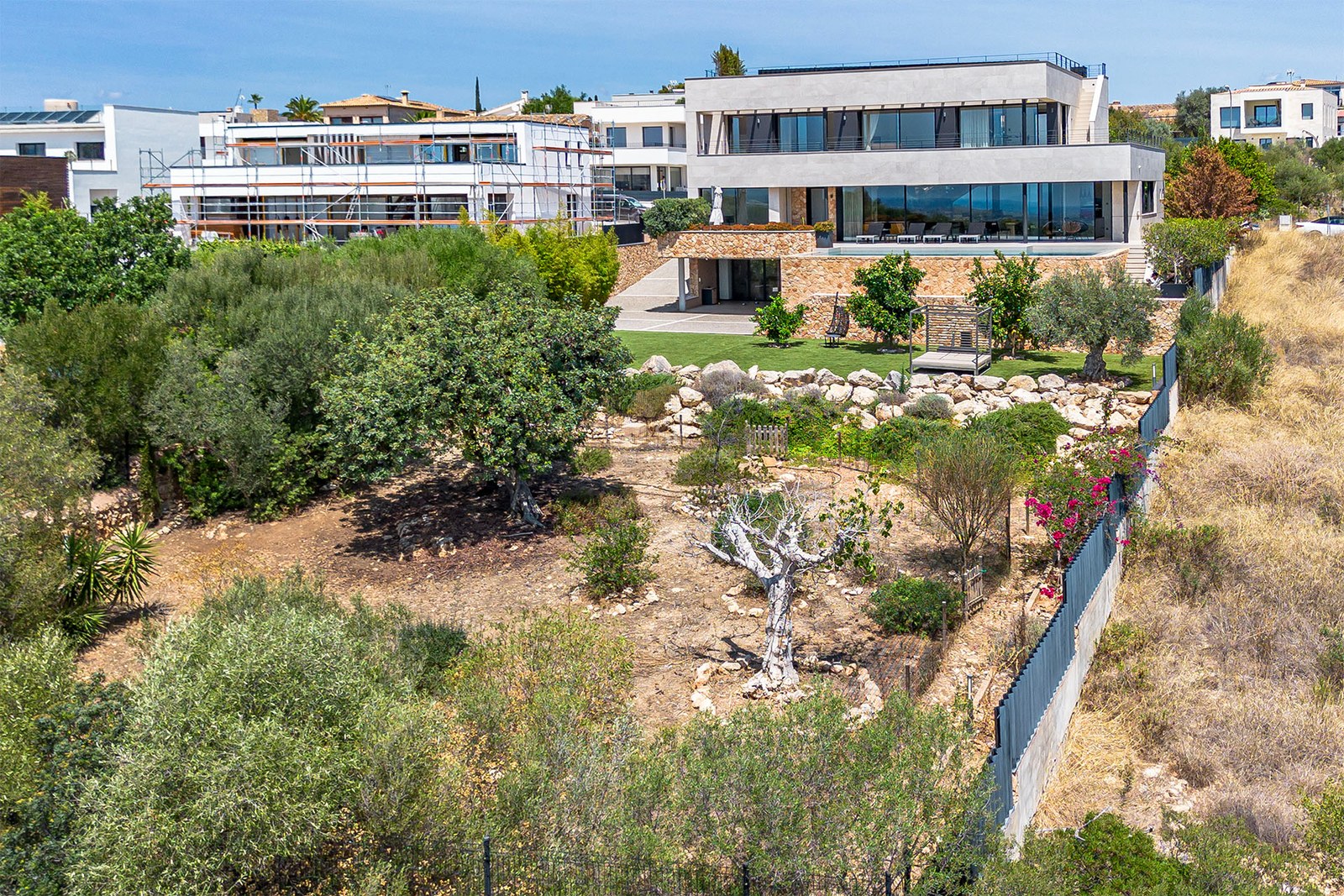 Side view of contemporary villa with tiered gardens and natural stone walls against a blue sky.