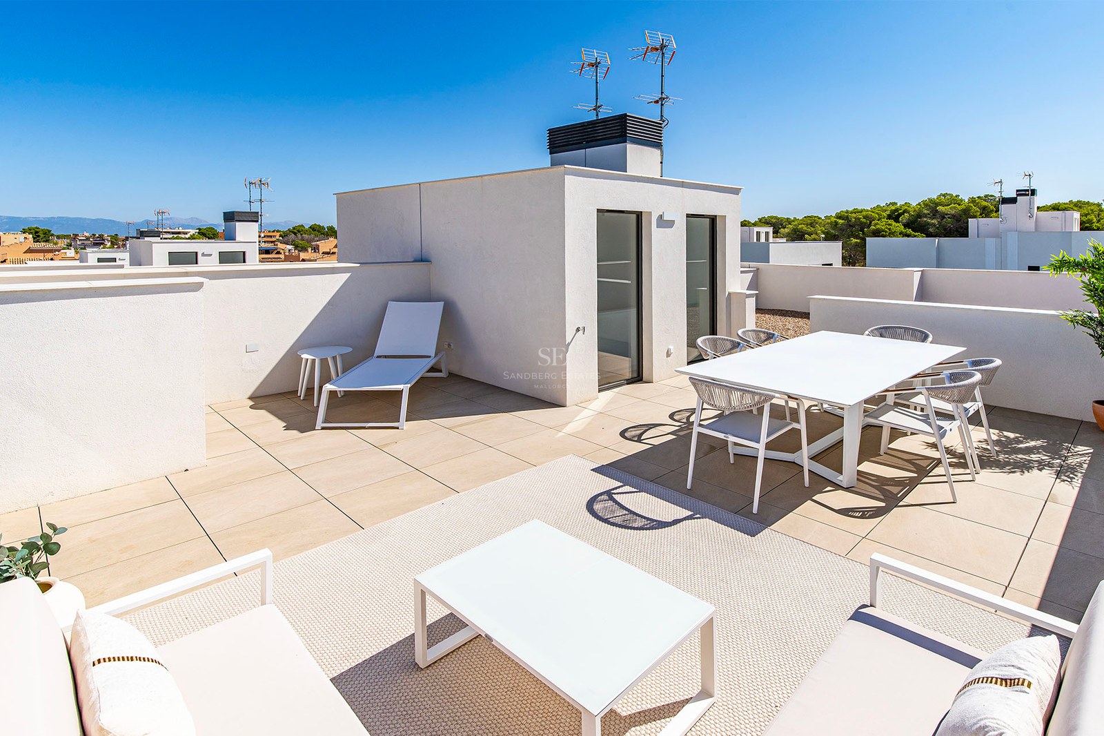 Terraza moderna soleada con muebles blancos, zona de comedor, área de descanso y suelos en tonos neutros.