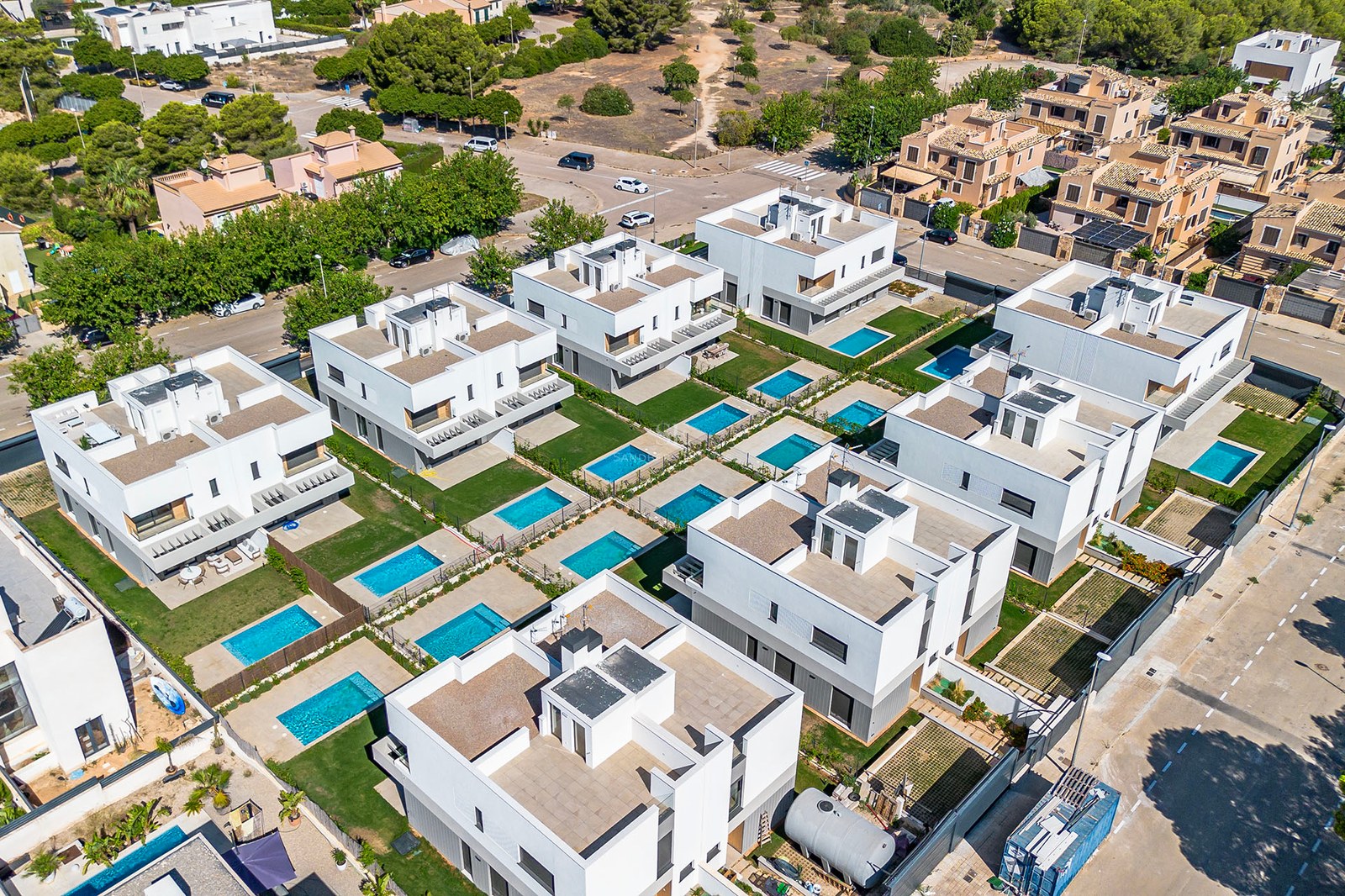 Vista aérea de una urbanización residencial contemporánea con villas blancas, jardines privados y piscinas individuales.