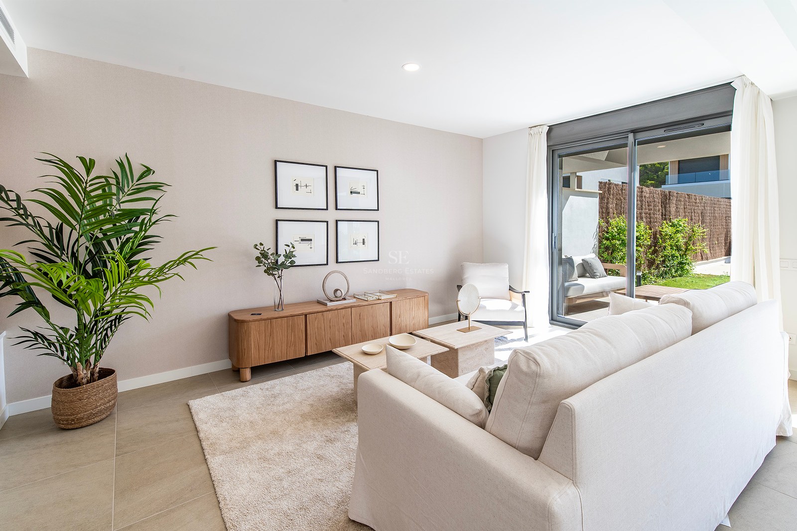 Salón contemporáneo con sofá crema, aparador de madera y puertas correderas de cristal hacia el jardín.