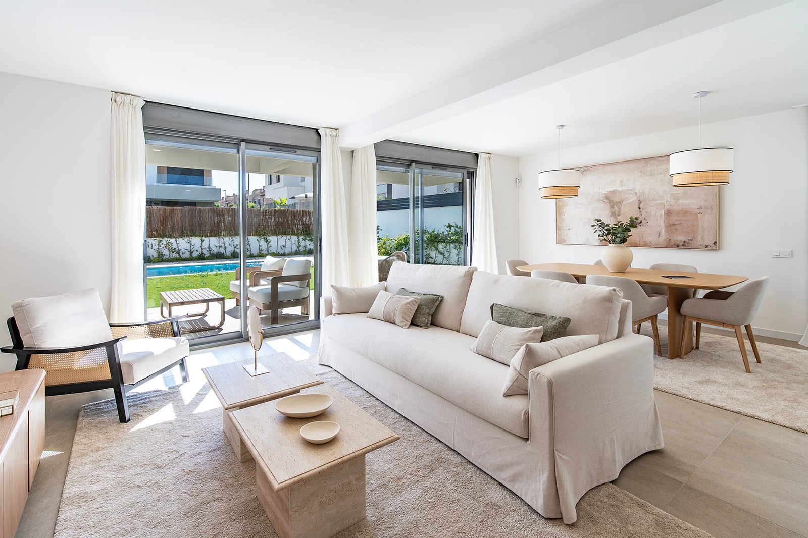 Salón moderno con sofá crema, mesas de piedra y ventanales con vistas a la piscina y el jardín privado.