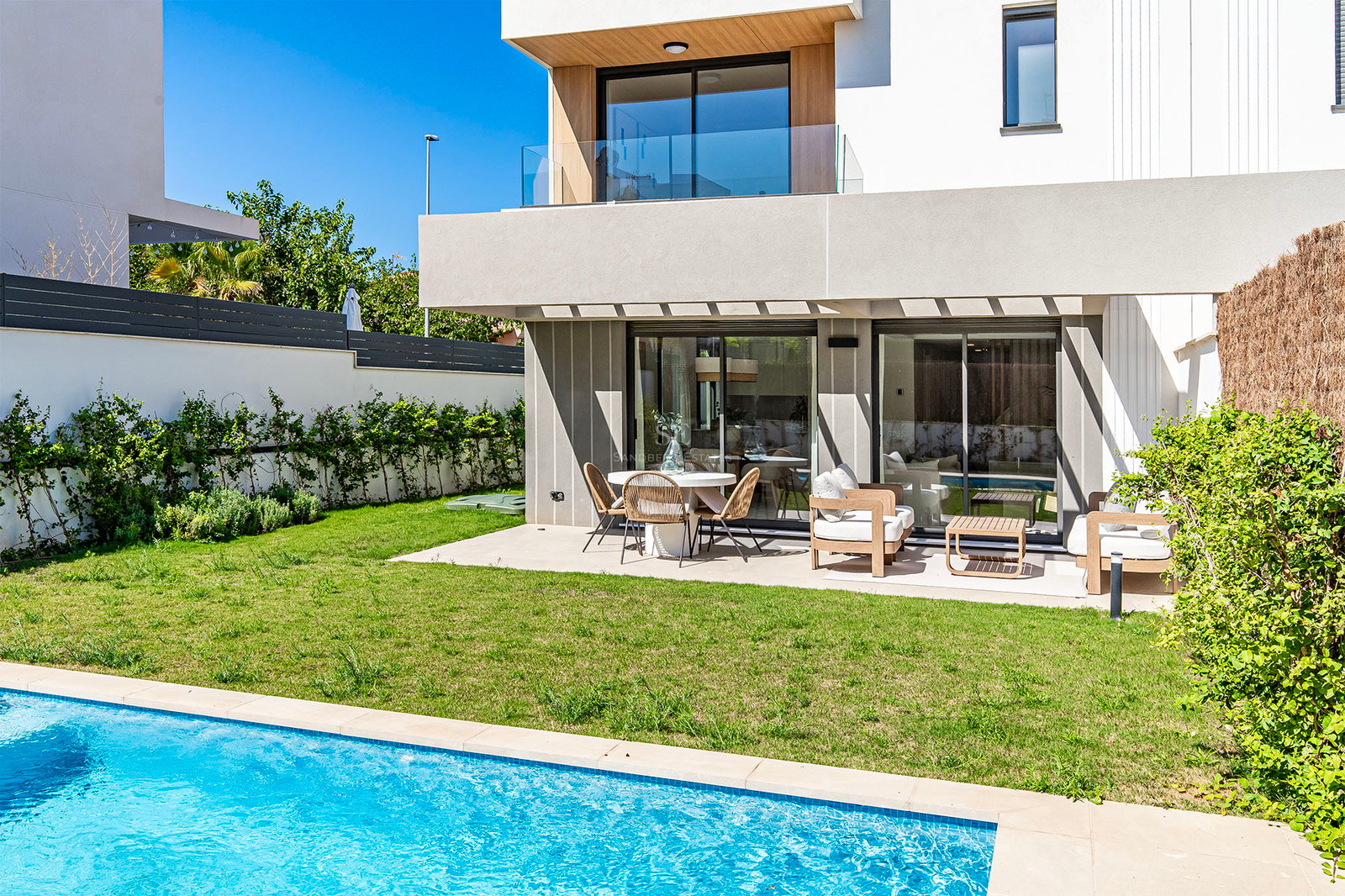 Villa contemporánea con piscina turquesa, césped cuidado y terraza sombreada con mobiliario de diseño.