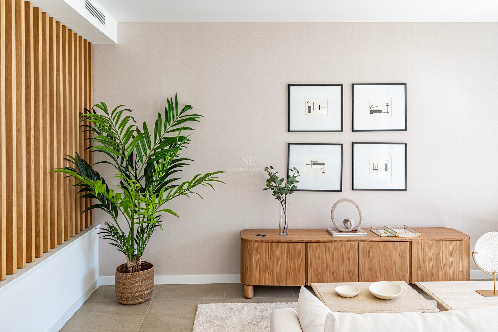 Detalle de salón con panelado de madera, aparador de roble, planta de interior y cuadros minimalistas.