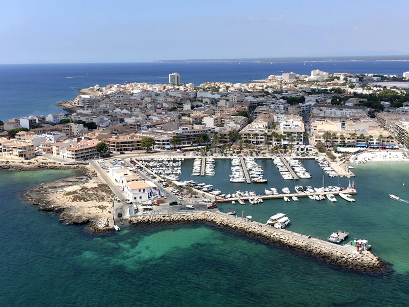 High-angle aerial shot of a Mediterranean marina with white boats and turquoise water next to a coastal town.