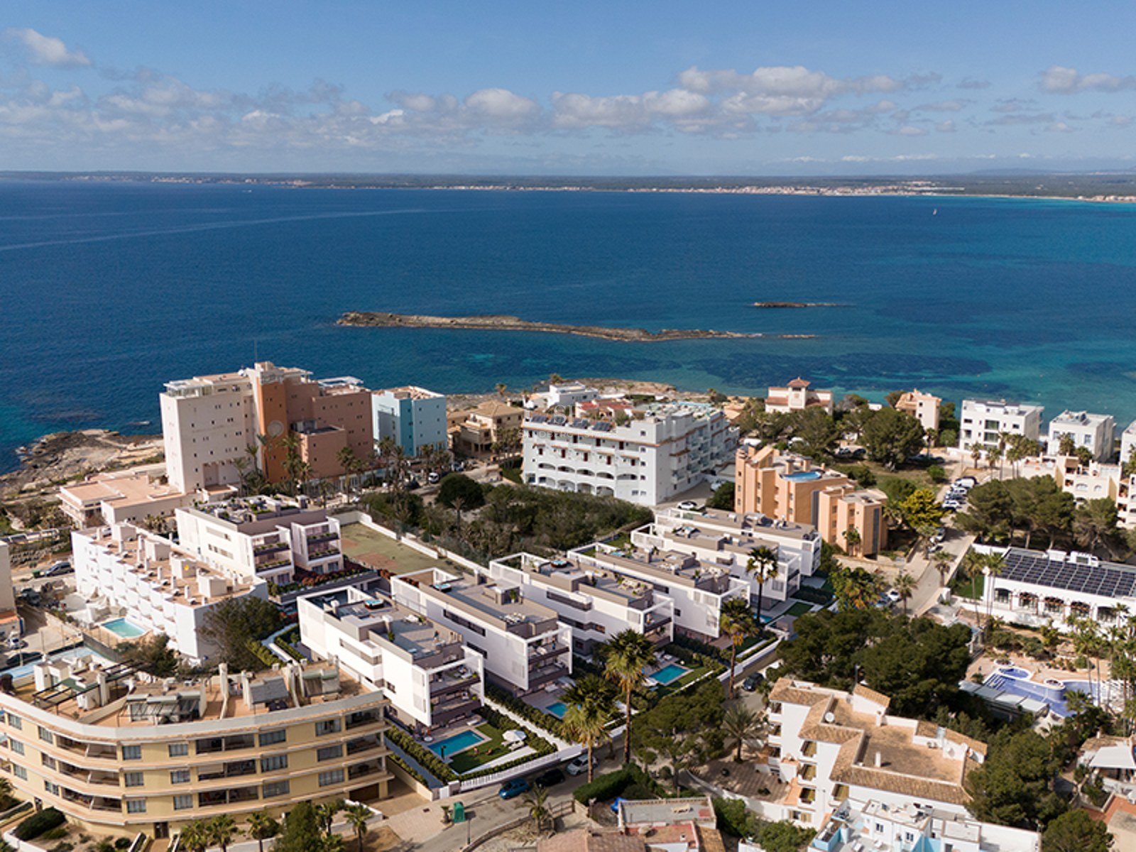 Aerial drone view of white modern apartment buildings along a turquoise Mediterranean coastline with blue sky.