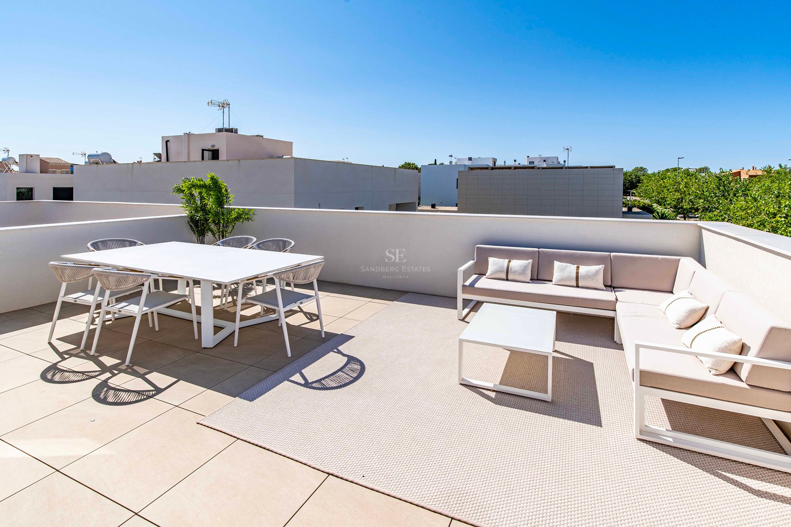 Sonnige Dachterrasse mit weißer Essgruppe und beigem Ecksofa unter strahlend blauem Himmel.