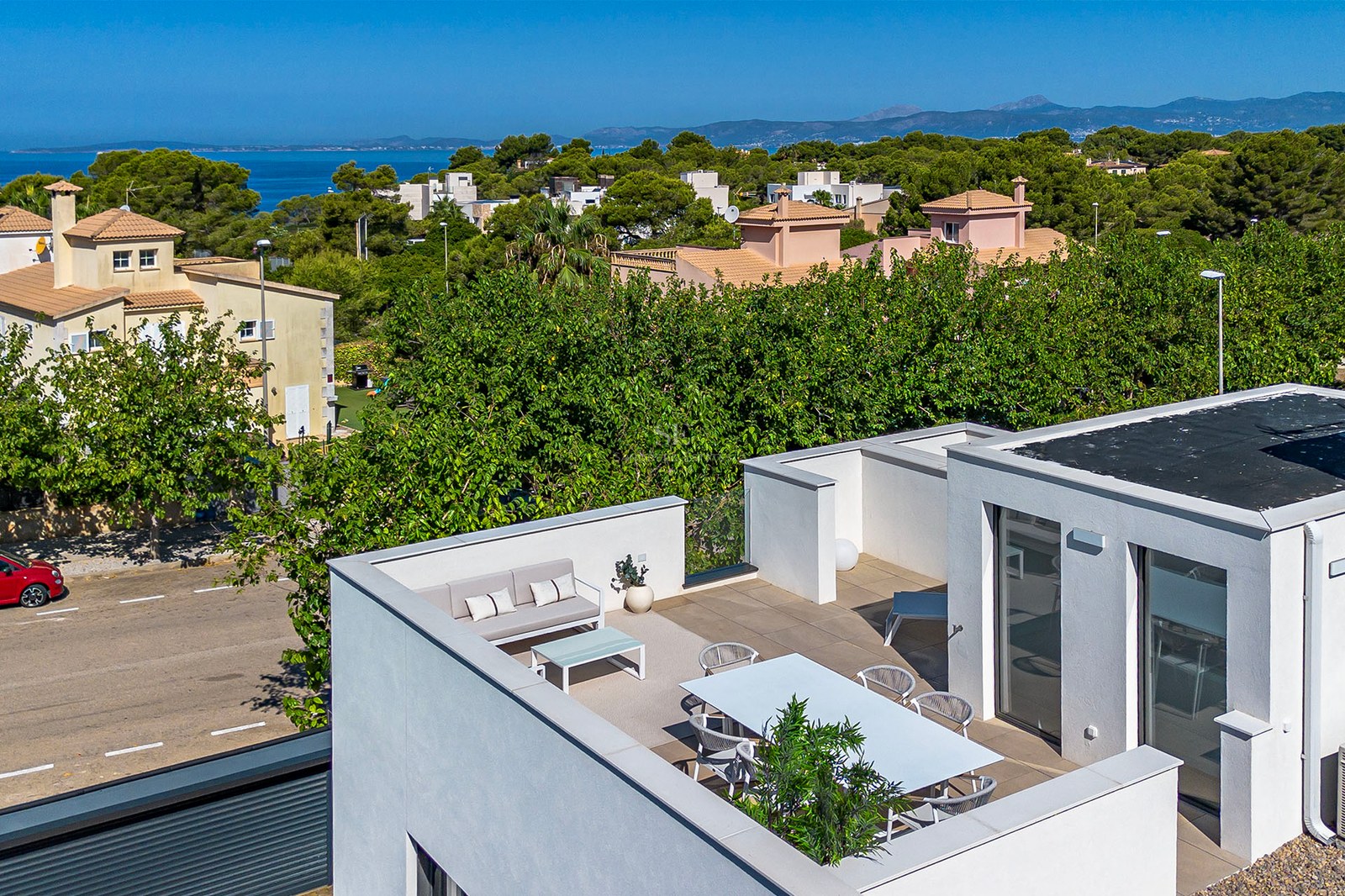 Moderne weiße Dachterrasse mit Essbereich und Loungemöbeln mit Blick auf das Mittelmeer und Pinienbäume.