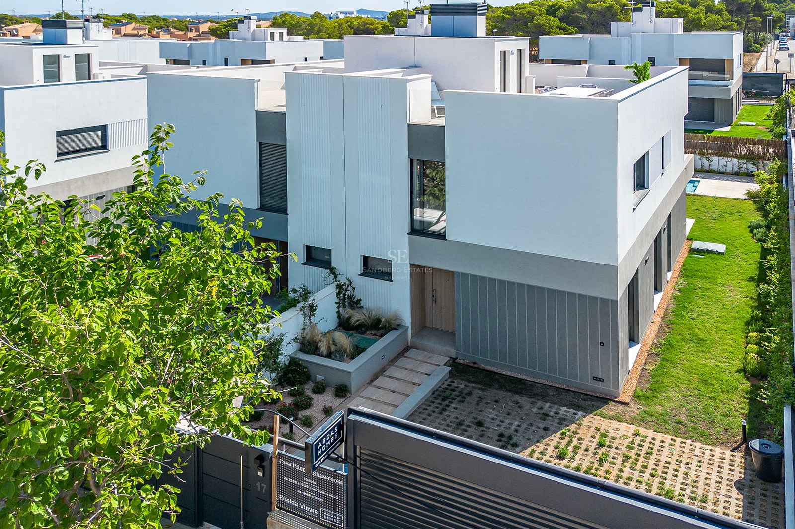 Außenansicht einer modernen weiß-grauen Villa mit Dachterrasse und gepflegtem Eingangsbereich bei Tageslicht.