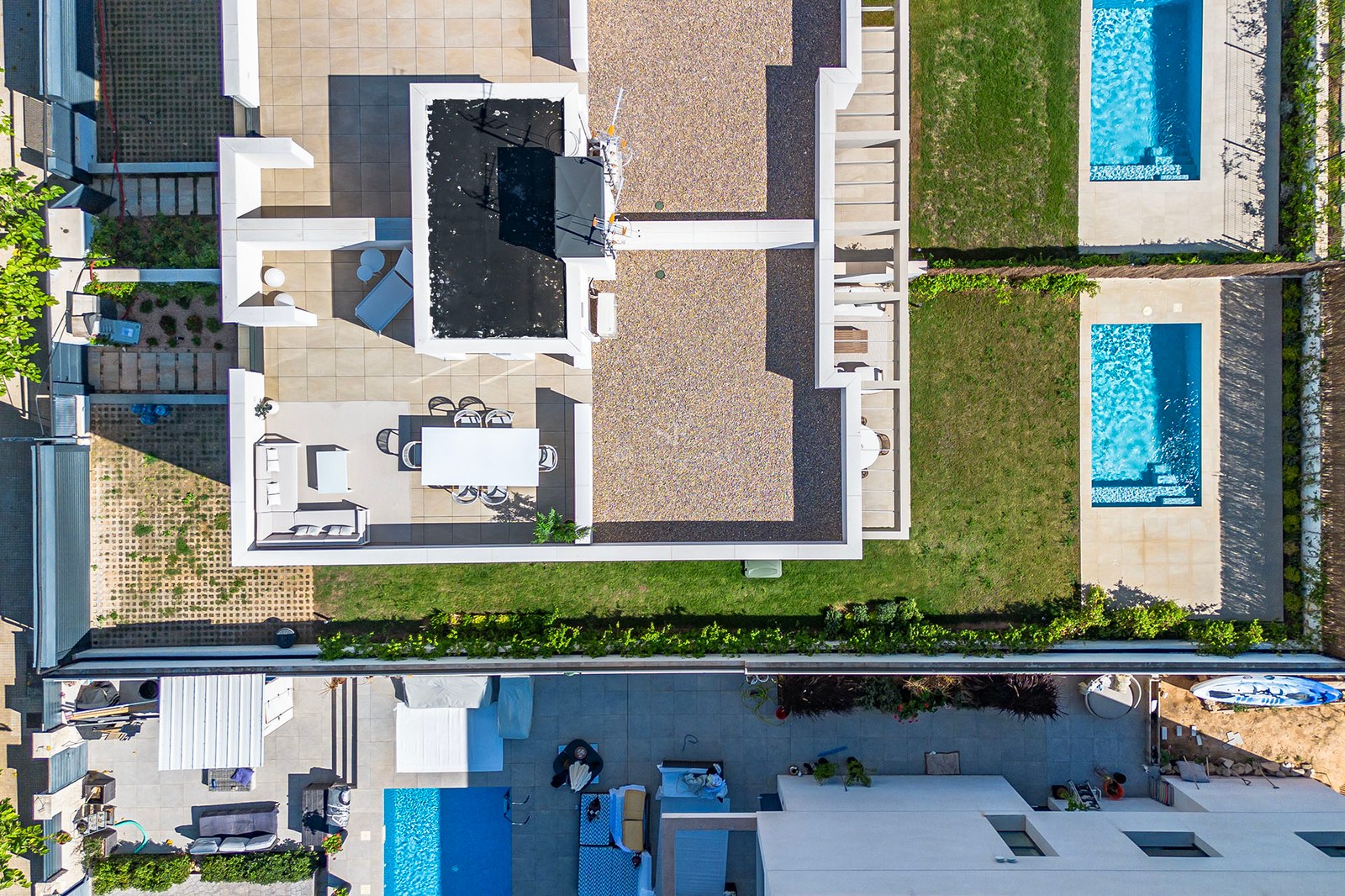 Draufsicht einer modernen Villa mit weißen Terrassen, Rasenflächen und zwei türkisfarbenen Pools.