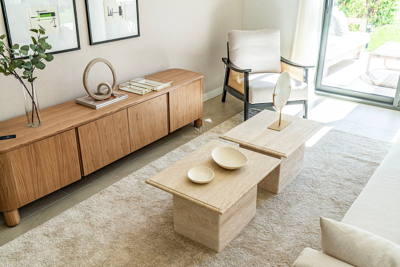Modernes Wohnzimmer mit Holz-Sideboard, Couchtischen aus Travertin und Wiener Geflecht-Sessel am Fenster.