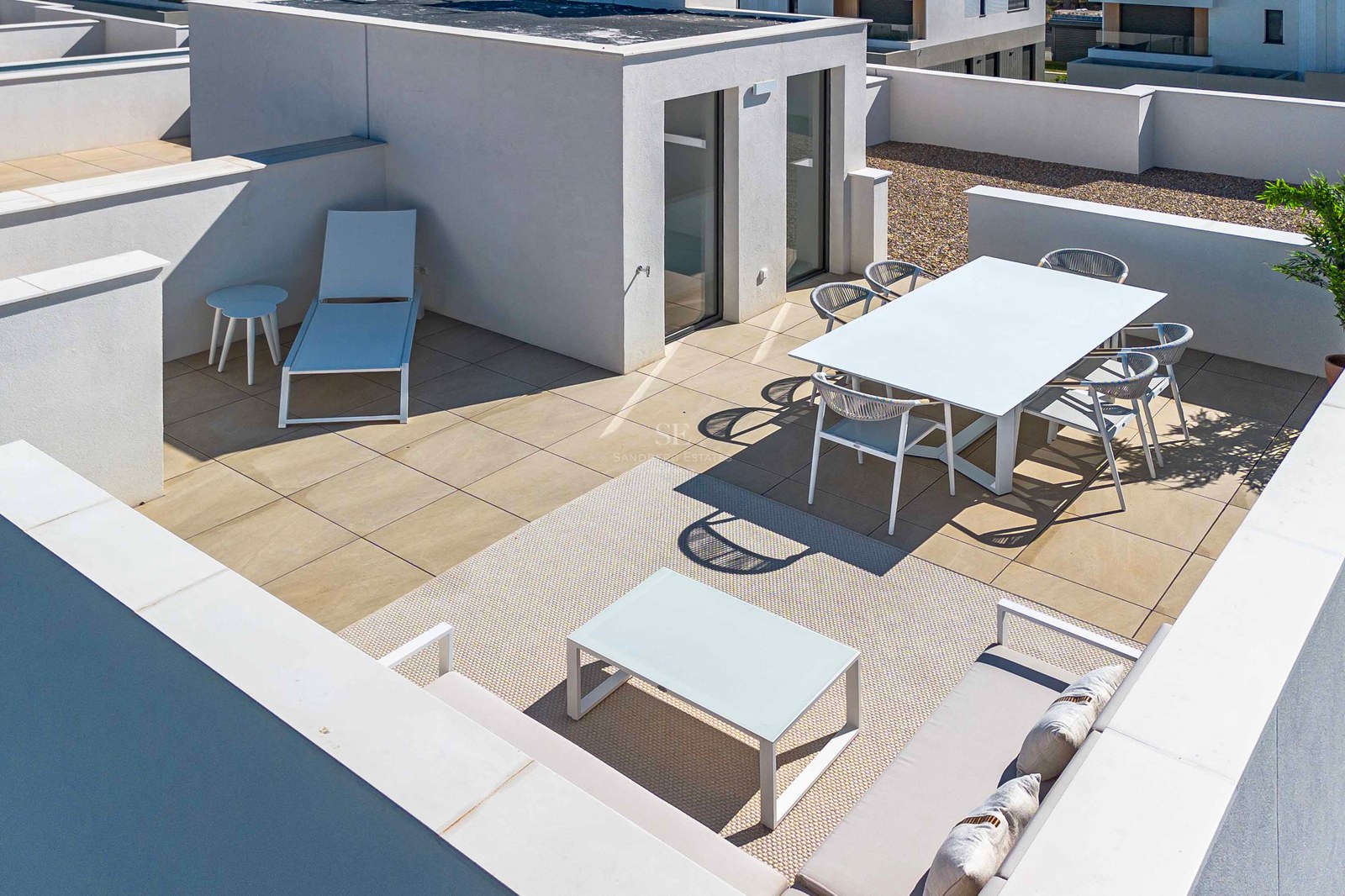 Moderne weiße Dachterrasse mit Esstisch, Sonnenliege und Loungebereich auf hellen Steinfliesen.